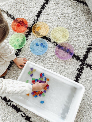 Gekleurde sorteerstenen 60 stuks - yourlittlefamily-nl - Deze gekleurde stenen liggen op een mat met gekleurde bakjes.
