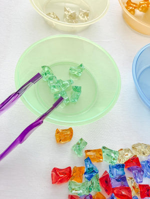 Gekleurde sorteerstenen 60 stuks - yourlittlefamily-nl - Sorteerstenen in een groen bakje met een pincet.